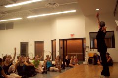 Students sit on the floor of a dance classroom watching OCU professor of dance Jo Rowan teach.